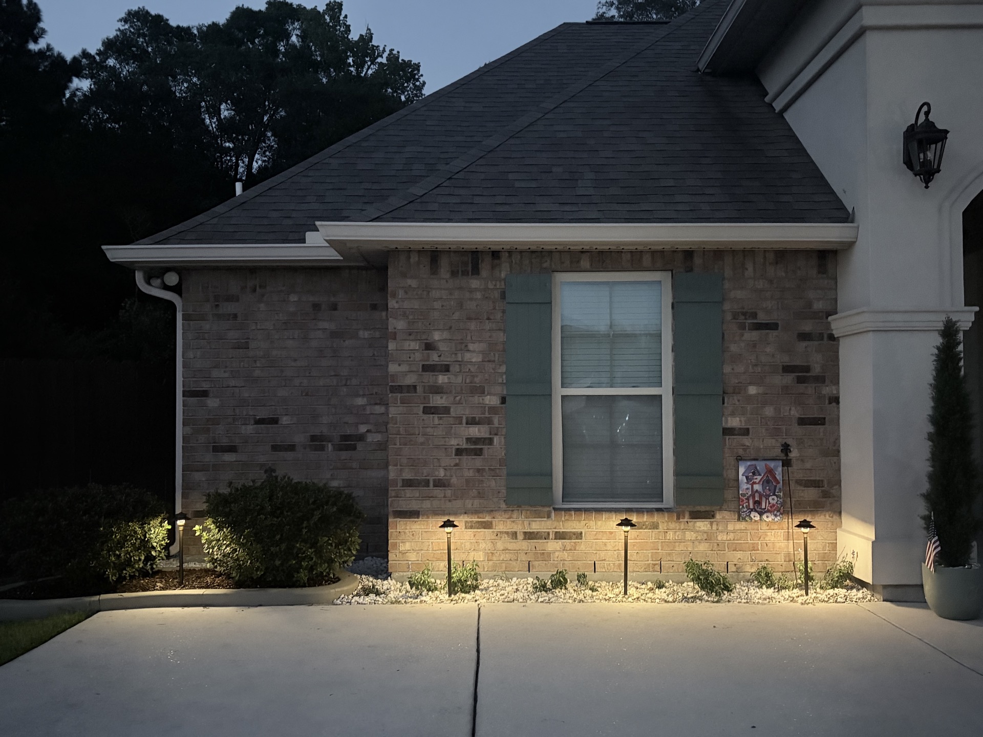 Brick building exterior at dusk with a row of low path lights illuminating a foundation planting bed