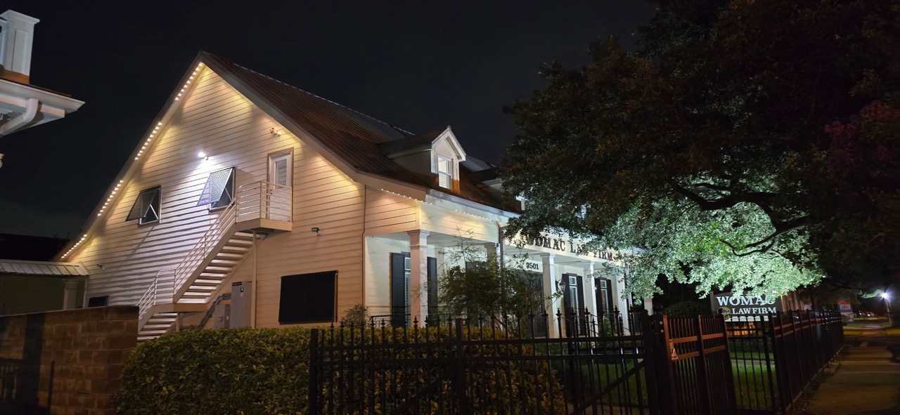 Historic two-story law firm building at night with warm white roofline and gable track lighting and an uplit oak tree beside the entrance sign